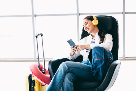 Lovely woman with headphones relaxing at airport lounge while browsing mobile phone before travel departure