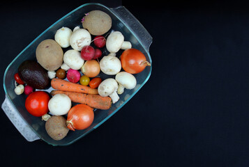 Vegetables lie in a glass container on a black background
