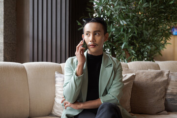 Portrait of nonbinary genderfluid young Asian gay businessman using phone in cafe