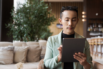 Portrait of nonbinary genderfluid young Asian gay man using digital tablet computer