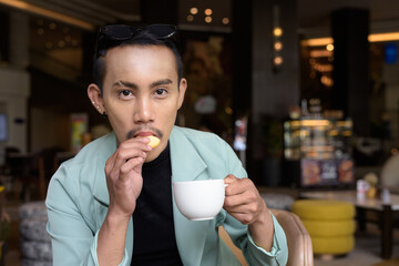 Portrait of nonbinary genderfluid young Asian gay man drinking coffee