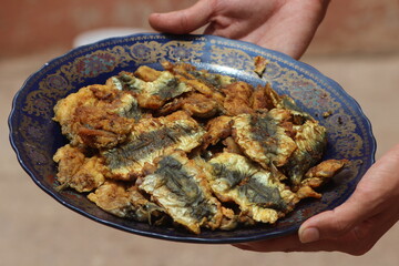 Hands holding a plate with fried sardines