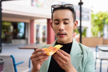 Portrait of nonbinary genderfluid young Asian gay man eating pizza ourdoors
