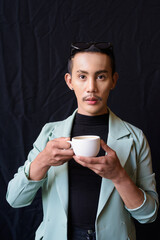 Portrait of nonbinary genderfluid young Asian gay man in studio holding coffee cup