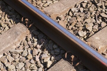 Rusty rail fastened to concrete sleepers with gravel ballast in sunlight