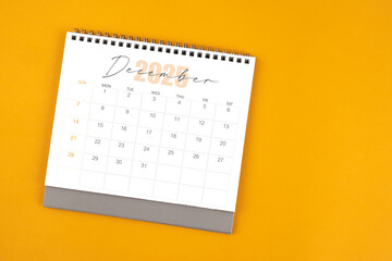 Top view of December 2025 desk calendar on yellow color background.