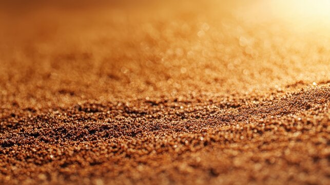 Close-up of fine golden sand grains sparkling under warm sunlight, creating a textured and shimmering surface.