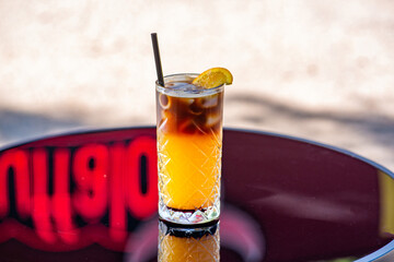 Espresso tonic cocktail in a glass glass with a straw on a table on a summer terrace in a cafe