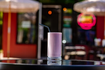 Milky pink shake with strawberry syrup on a table on a summer terrace in a cafe