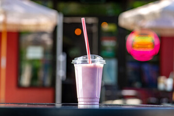 Milky pink shake with strawberry syrup to go on a table on a summer terrace in a cafe