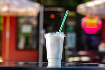 White Milky shake in a tall glass with a straw on a table on a summer terrace in a cafe