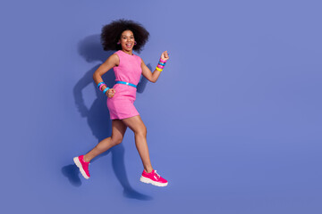 Smiling young woman in a pink dress jumping with joy against a vibrant purple background, embracing...
