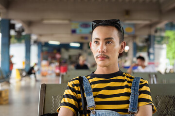 Portrait of nonbinary genderfluid young Asian gay tourist man in bus terminal