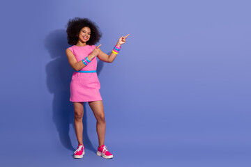 Young woman in a pink dress pointing playfully against purple background showcasing retro style and...