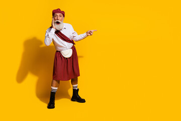Elderly man in traditional Scottish attire gestures passionately against a vibrant yellow background showcasing culture and fun