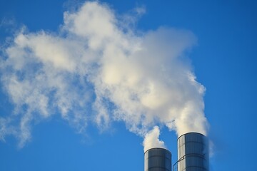 Industrial chimneys emitting white smoke into clear blue sky symbolizing air pollution and environmental impact