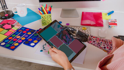 Creative artist using tablet with prosthetic hand in colorful, organized digital workspace