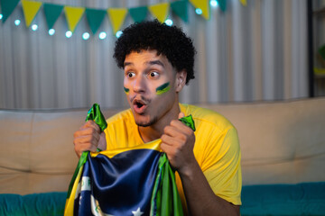 Male soccer fan with Brazilian face paint and yellow shirt watching intensely while clutching a...