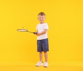 Little boy with badminton racket and shuttlecock on yellow background