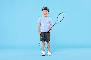 Little boy with badminton rackets on light blue background