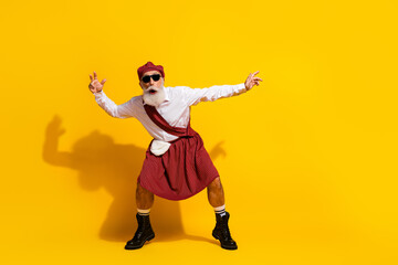 Stylish elderly man in traditional Scottish attire posing with cheerful gestures against a vibrant yellow backdrop