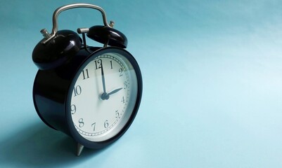 Round black vintage alarm clock isolated on turquoise background.