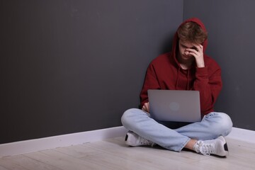 Cyber bullying. Upset teenage boy with laptop on floor indoors. Space for text