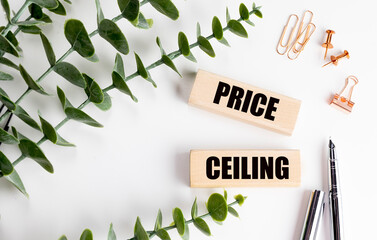 Wooden blocks with words price ceiling on white desk with leaves, pens and stationery items