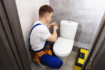Professional plumber fixing toilet bowl in restroom