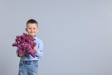 Little boy with bouquet of lilac flowers on light grey background, space for text