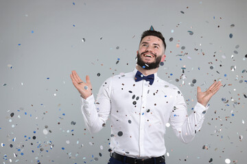 Happy Birthday. Handsome man with party hat under confetti shower on grey background, space for text