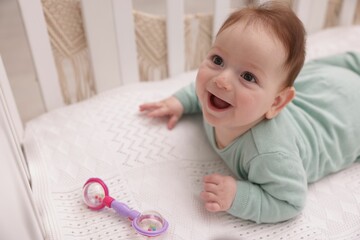 Cute little baby with rattle toy in crib at home