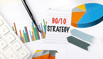 Card with 90 10 strategy text on desk with charts, pie graphs, pen, calculator and paper arrows