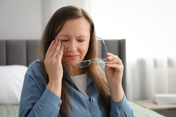 Woman with glasses suffering from eyestrain on bed at home