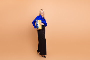 Senior businesswoman holding colorful folders in a professional outfit on beige background...