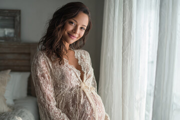 Fototapeta premium Maternity Moment With Young Pregnant Hispanic Woman in Bright Bedroom by Window