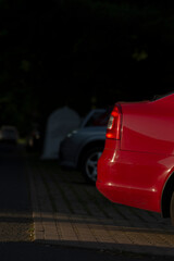 In a dimly lit parking lot, there is a red car parked, standing out amidst the shadows and...