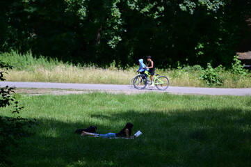 A young woman lies in the grass of park in Berlin on a warm summer day while she reads a book. 