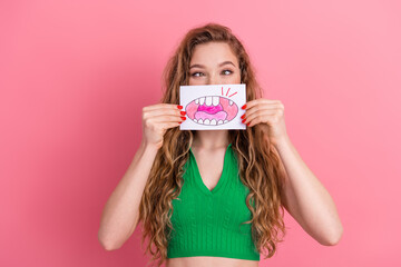 Young woman playfully holding drawing of lips on pink background, wearing green top, showcasing...