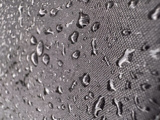 Close-up of water droplets on a waterproof fabric surface. The tightly woven texture and water...