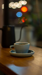 Cup of hot coffee or tea and teapot on wooden table with bokeh background