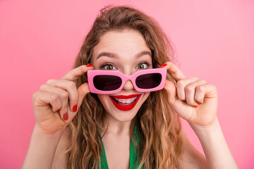 Stylish young woman with pink sunglass smiling confidently against bright pink background in a playful gesture