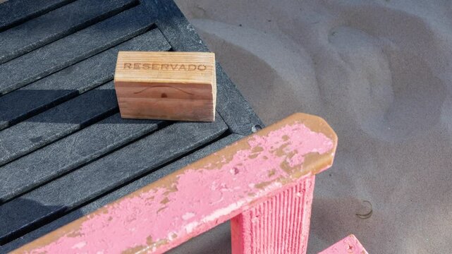 Wooden reservado sign on grey slatted table next to weathered pink chair on sandy beach