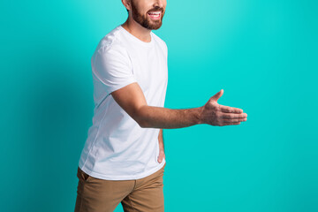 Fototapeta premium Smiling man extends hand for a handshake against a teal backdrop wearing casual fashion showcasing a friendly gesture