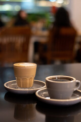 A cup of coffee and a glass of coffee latte with froth art on the table