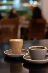 A cup of coffee and a glass of coffee latte with froth art on the table