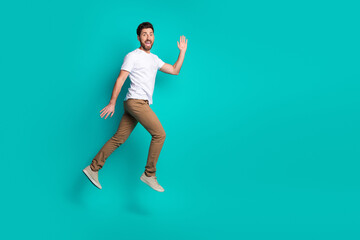 Young man jumping energetically against a solid turquoise background while expressing happiness with a cheerful wave