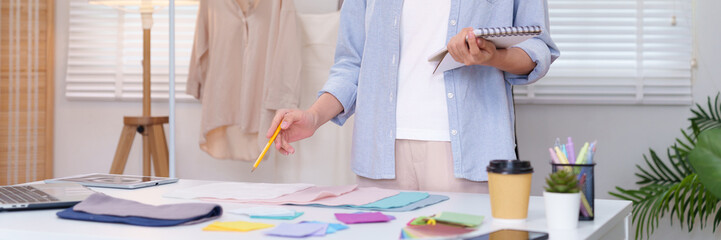 Asian adult fashion designer working with fabric samples in studio creates trendy apparel...