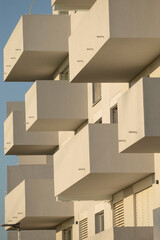 A tall building adorned with numerous balconies and featuring a vibrant blue sky as its backdrop,...