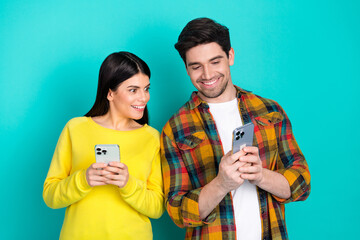 Young couple using smartphones in a cheerful interaction against bright turquoise background,...